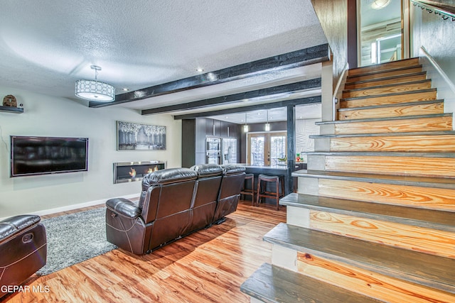 living area featuring a textured ceiling, wood finished floors, french doors, stairway, and beam ceiling