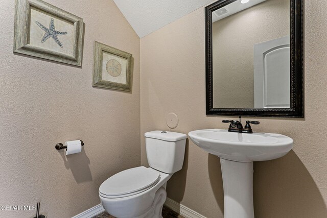 bathroom featuring lofted ceiling, baseboards, a textured wall, and toilet