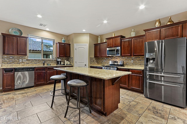 kitchen featuring a center island, stainless steel appliances, visible vents, backsplash, and a kitchen breakfast bar