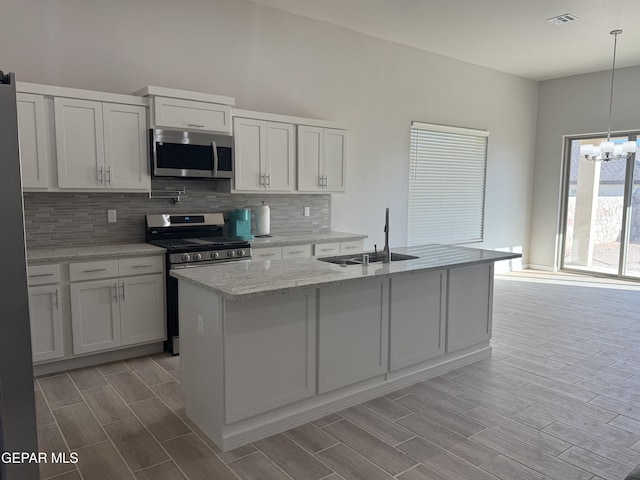 kitchen featuring stainless steel appliances, a sink, visible vents, hanging light fixtures, and light stone countertops