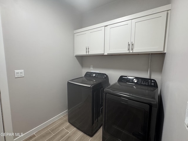 clothes washing area featuring cabinet space, baseboards, wood finish floors, and washing machine and clothes dryer