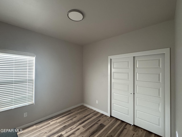 unfurnished bedroom featuring a closet, dark wood-style flooring, and baseboards