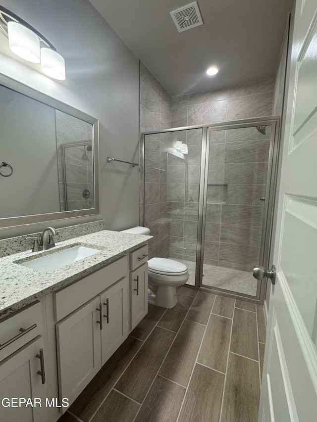 bathroom with toilet, vanity, visible vents, a shower stall, and wood tiled floor