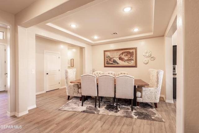 dining space featuring a raised ceiling, visible vents, baseboards, and wood finished floors