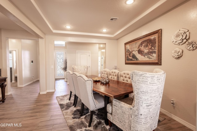 dining area with a raised ceiling, wood finished floors, visible vents, and baseboards