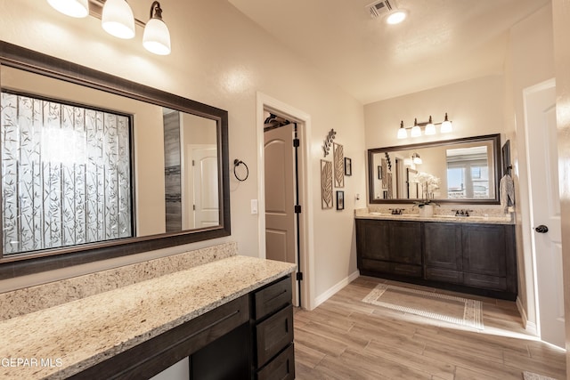 full bath featuring double vanity, baseboards, visible vents, wood finish floors, and a sink