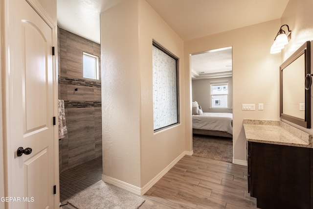 ensuite bathroom featuring a walk in shower, wood finished floors, vanity, baseboards, and ensuite bath