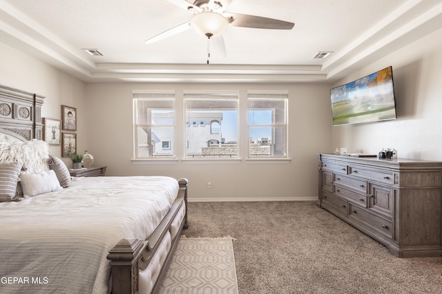 bedroom with a tray ceiling, light carpet, visible vents, and baseboards