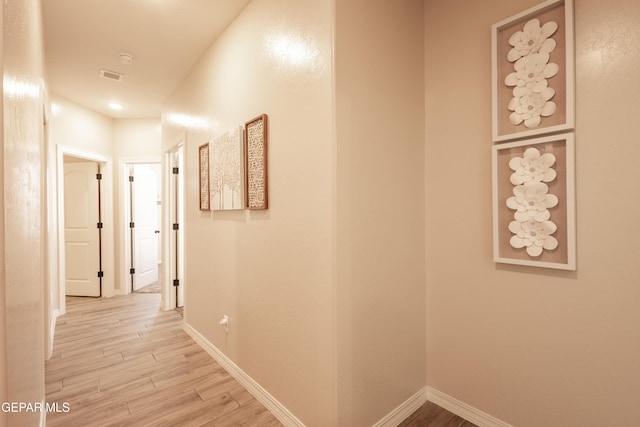 hall featuring light wood-type flooring, visible vents, and baseboards