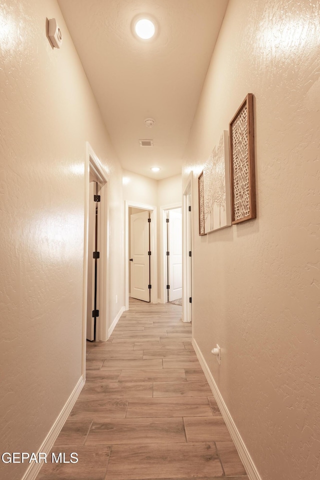 hall with wood tiled floor, visible vents, a textured wall, and baseboards