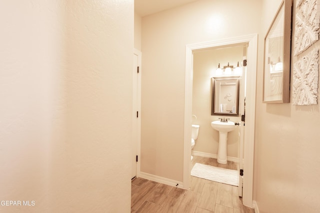 hall with light wood-type flooring, baseboards, and a sink