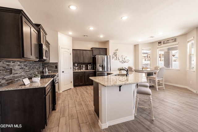 kitchen featuring stainless steel appliances, light wood-style flooring, a sink, dark brown cabinetry, and a kitchen bar