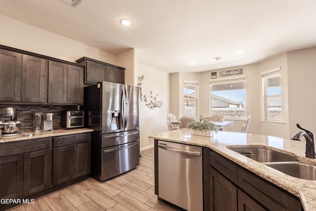 kitchen featuring light wood finished floors, tasteful backsplash, appliances with stainless steel finishes, a sink, and dark brown cabinets