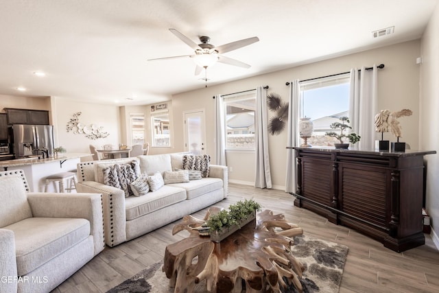 living room featuring a ceiling fan, light wood-type flooring, visible vents, and baseboards