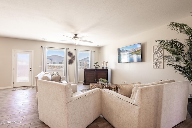 living area with ceiling fan, a textured ceiling, wood finished floors, visible vents, and baseboards