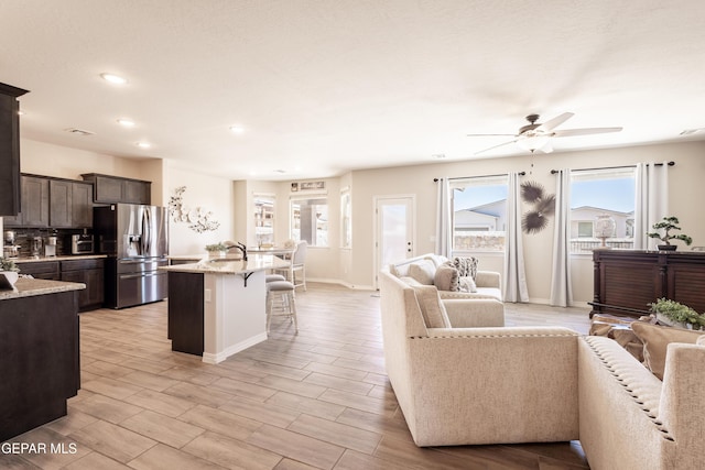 kitchen featuring dark brown cabinetry, stainless steel fridge, open floor plan, a healthy amount of sunlight, and a kitchen bar