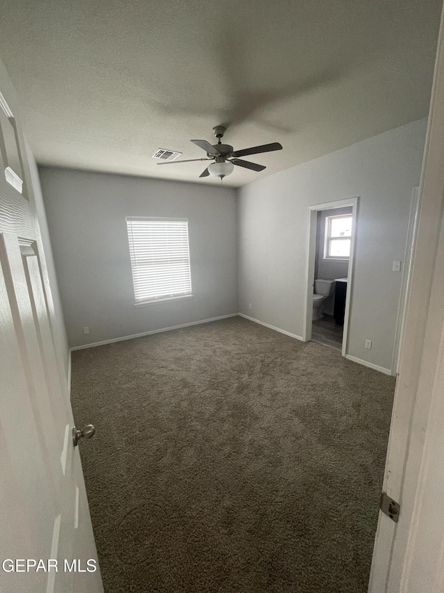 unfurnished room with a textured ceiling, visible vents, baseboards, a ceiling fan, and dark colored carpet