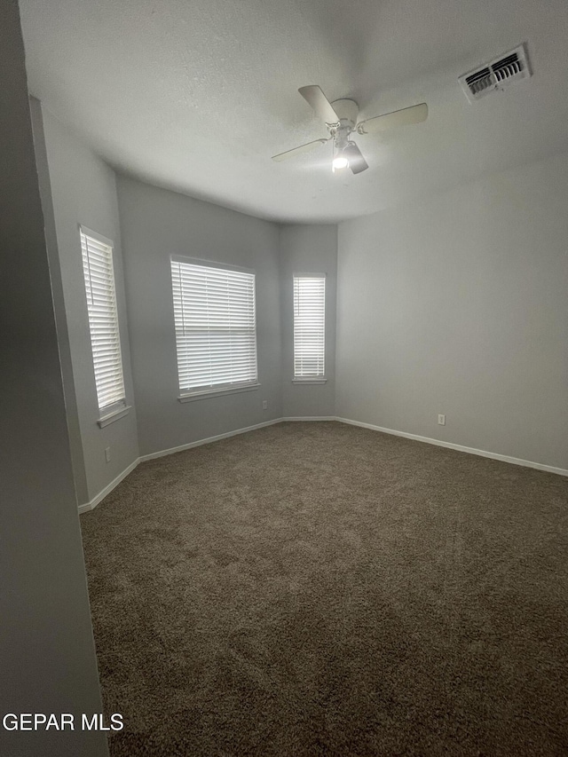 unfurnished room featuring baseboards, visible vents, dark colored carpet, and a ceiling fan