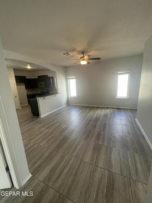 unfurnished living room with baseboards, a textured ceiling, visible vents, and a ceiling fan