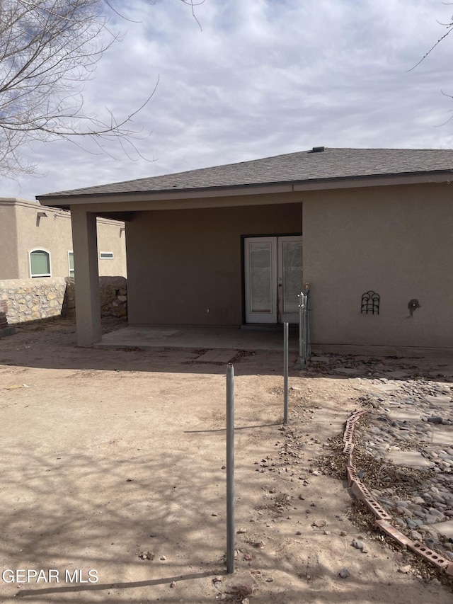 rear view of house featuring a shingled roof and stucco siding