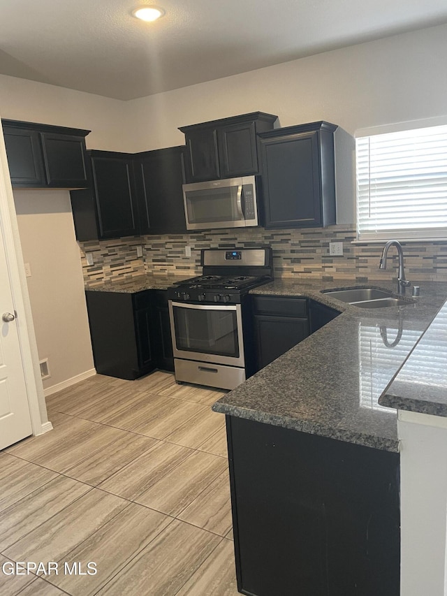 kitchen featuring appliances with stainless steel finishes, dark stone counters, a sink, and dark cabinets