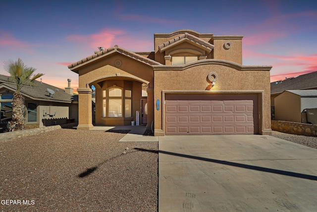 mediterranean / spanish home with a garage, driveway, a tiled roof, and stucco siding