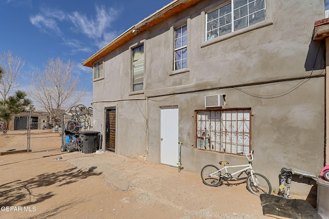 back of property featuring a wall mounted AC, fence, a gate, and stucco siding