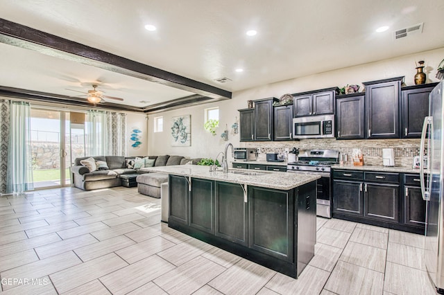 kitchen with tasteful backsplash, an island with sink, appliances with stainless steel finishes, open floor plan, and a sink