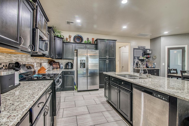 kitchen with light stone countertops, a sink, visible vents, appliances with stainless steel finishes, and decorative backsplash