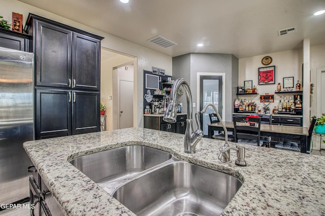 kitchen with light stone counters, visible vents, a sink, and stainless steel refrigerator