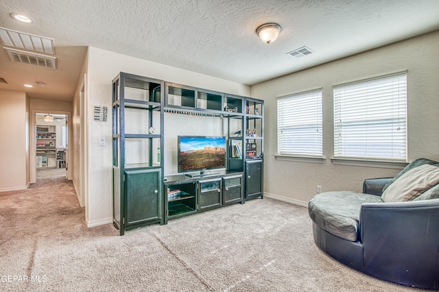 carpeted living area with a textured ceiling, a textured wall, visible vents, and baseboards