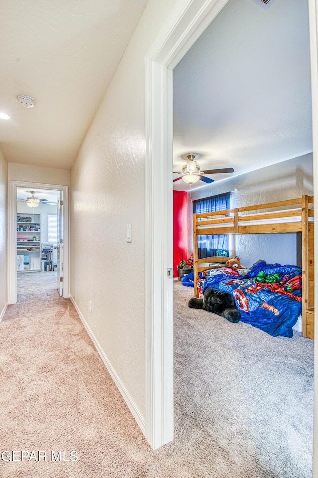 hall featuring carpet flooring, a textured wall, and baseboards