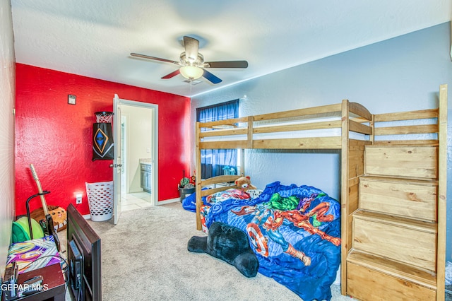 carpeted bedroom with a textured wall, ensuite bath, and a ceiling fan