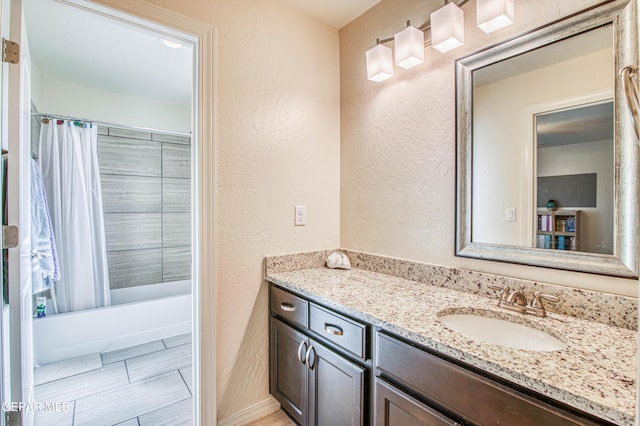 full bath with a textured wall, shower / bath combo, and vanity