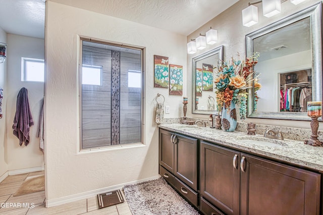 bathroom with double vanity, a textured wall, a walk in closet, a textured ceiling, and a sink