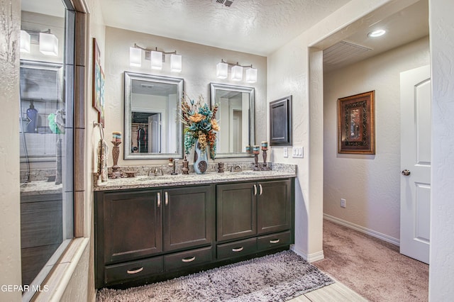 full bath with a textured ceiling, a textured wall, a sink, baseboards, and double vanity