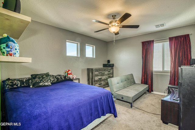 bedroom featuring light carpet, baseboards, visible vents, a textured wall, and ceiling fan