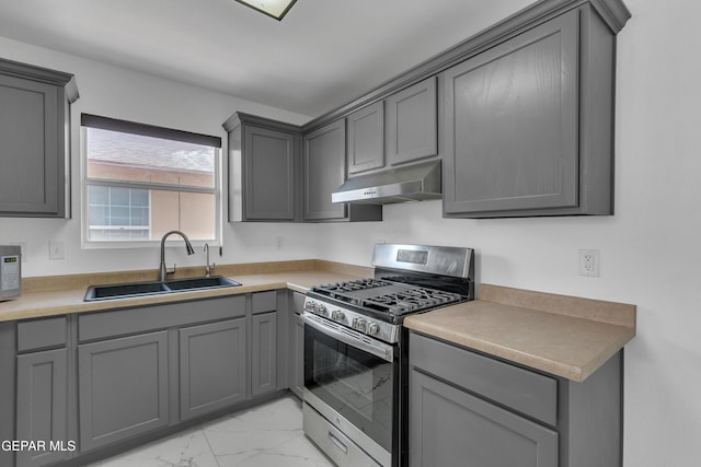 kitchen with marble finish floor, gray cabinetry, a sink, gas range, and under cabinet range hood