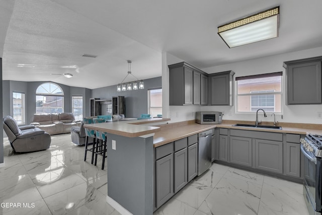 kitchen with appliances with stainless steel finishes, a sink, marble finish floor, gray cabinetry, and a wealth of natural light