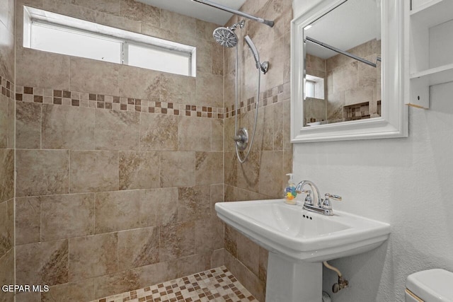 bathroom with toilet, a sink, and tiled shower