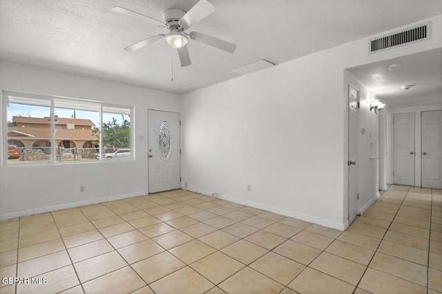 empty room featuring light tile patterned floors, visible vents, a ceiling fan, a textured ceiling, and baseboards