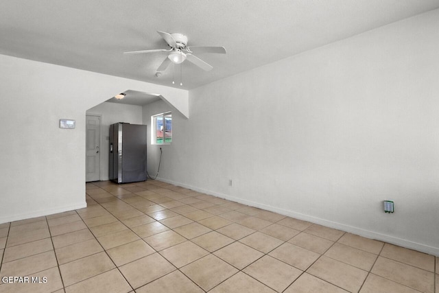 unfurnished room featuring a ceiling fan, arched walkways, light tile patterned flooring, and baseboards