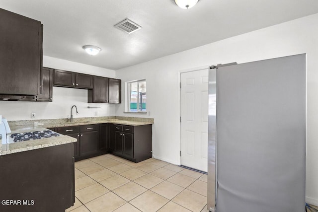 kitchen featuring light tile patterned floors, visible vents, freestanding refrigerator, dark brown cabinets, and a sink