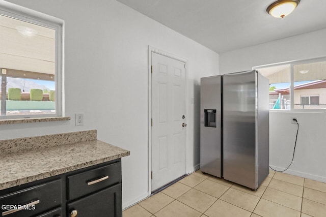 kitchen featuring dark cabinets, a healthy amount of sunlight, stainless steel fridge with ice dispenser, and light tile patterned floors