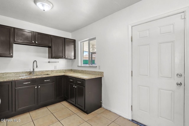 kitchen featuring light stone countertops, a sink, dark brown cabinets, and light tile patterned floors