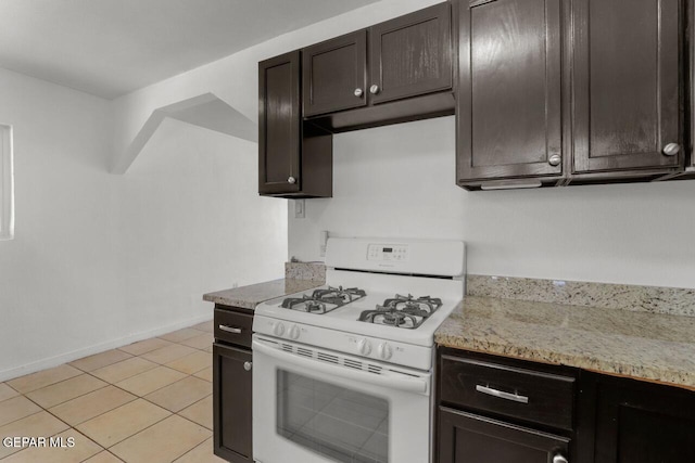 kitchen featuring white range with gas stovetop, baseboards, light stone counters, dark brown cabinets, and light tile patterned flooring