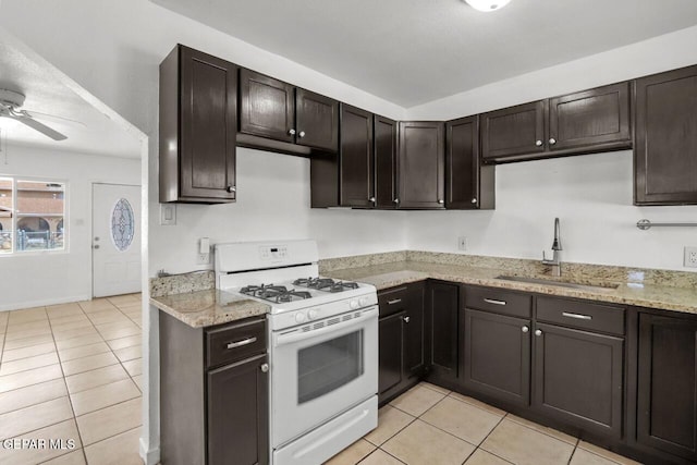 kitchen with a sink, light tile patterned floors, dark brown cabinets, and gas range gas stove