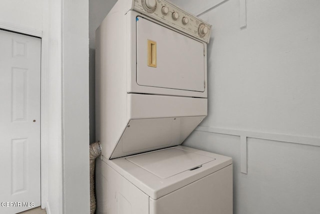 washroom with a wainscoted wall, stacked washer and dryer, laundry area, and a decorative wall