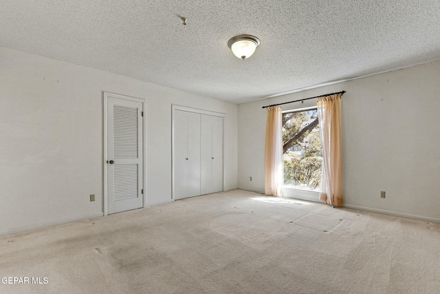 unfurnished bedroom with a textured ceiling, carpet floors, and two closets