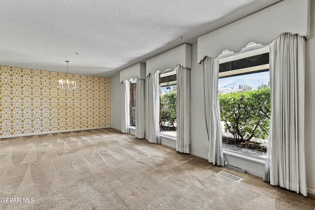 carpeted spare room with wallpapered walls, baseboards, visible vents, an inviting chandelier, and a textured ceiling